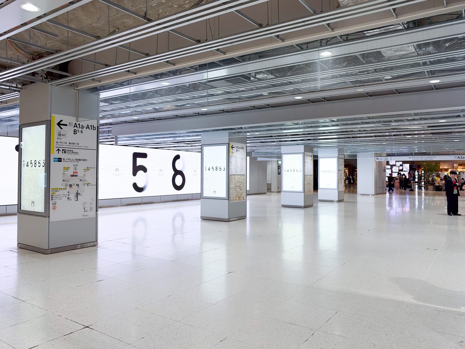 地下鉄コンコース（虎ノ門ヒルズ駅）。柱のデジタルサイネージに「56」の大きな数字。広告祭関連のビジュアルが並ぶ。遠くに出口への通路